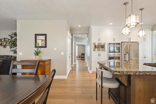 Kitchen featuring appliances with stainless steel finishes, light wood-style flooring, dark stone countertops, white cabinetry, and hanging light fixtures | Image 11