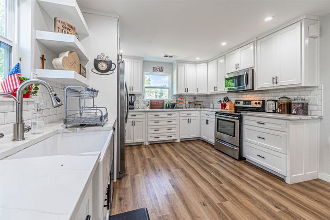 Kitchen featuring appliances with stainless steel finishes, open shelves, light wood finished floors, decorative backsplash, and white cabinetry | Image 11