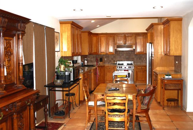 Kitchen with stainless steel appliances, under cabinet range hood, tasteful backsplash, brown cabinets, and light tile patterned floors | Image 14