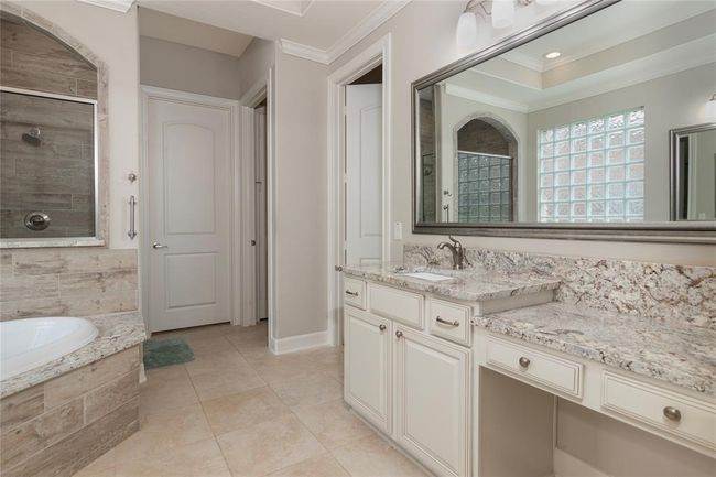 This spacious bathroom features a large framed mirror, and a built-in vanity. It includes a tiled walk-in shower and a separate bathtub, complemented by soft neutral tones and ample natural light. | Image 30