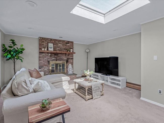 Living area featuring crown molding, light colored carpet, baseboards, a skylight, and a brick fireplace | Image 13