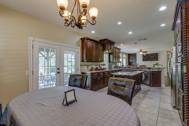 Kitchen featuring a kitchen island, appliances with stainless steel finishes, a chandelier, a ceiling fan, and dark brown cabinetry. Notice the double doors on the left, that lead to the backyard. | Image 16