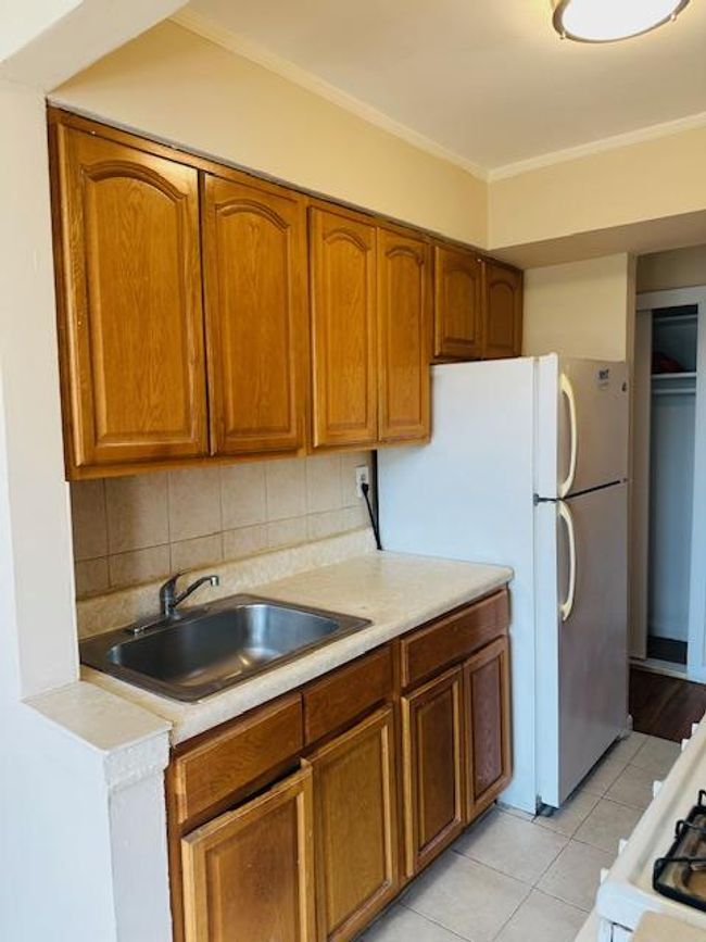 Kitchen featuring light countertops, brown cabinets, crown molding, light tile patterned floors, and decorative backsplash | Image 10
