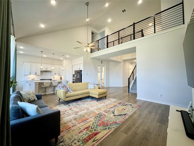 Living area featuring stairway, a ceiling fan, dark wood-type flooring, recessed lighting, and high vaulted ceiling | Image 4