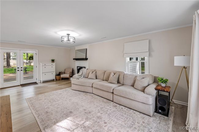 Living room with crown molding, baseboards, light wood-type flooring, a fireplace, and french doors | Image 8