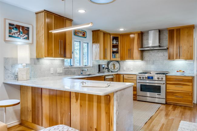 Kitchen featuring wall chimney range hood, a breakfast bar, kitchen peninsula, and appliances with stainless steel finishes | Image 13