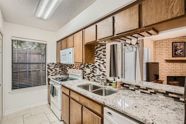 Kitchen featuring white appliances, decorative backsplash, a fireplace, a textured ceiling, and light stone countertops | Image 7
