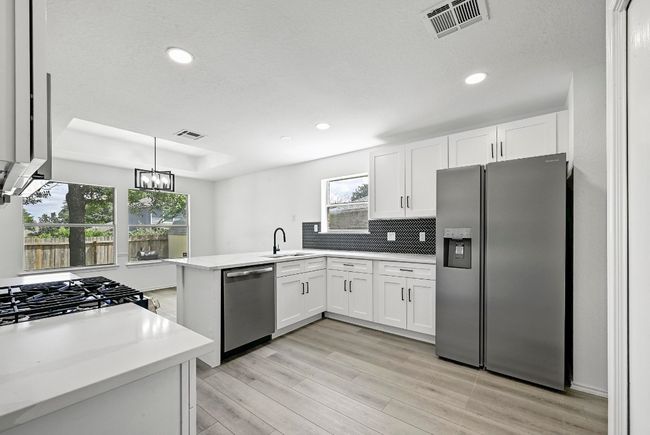 Kitchen with stainless steel appliances, a peninsula, white cabinets, light countertops, and recessed lighting | Image 12