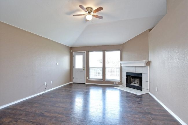 Unfurnished living room with a ceiling fan, a tiled fireplace, wood finished floors, vaulted ceiling, and a textured wall | Image 8
