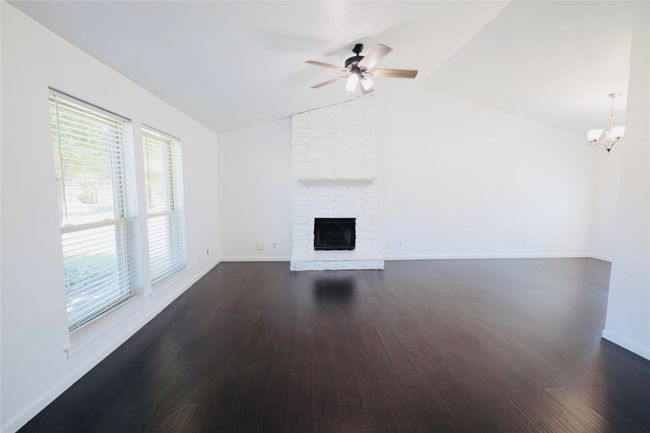 living room with vaulted ceiling, a ceiling fan, dark wood-style floors, a chandelier, and a brick fireplace | Image 6