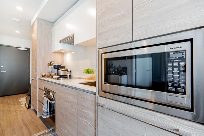 Kitchen with under cabinet range hood, stainless steel appliances, modern cabinets, and light countertops | Image 7