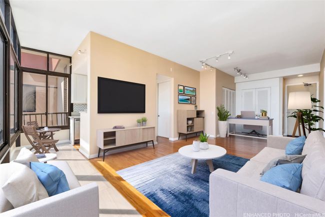 Enhanced. Virtually staged depicting a home office arrangement in the area near entry. Enclosed lanai is in foreground and runs the width of the condo. Kitchen is located behind the wall with television. | Image 4