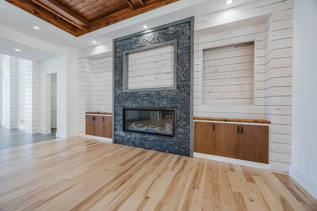 Unfurnished living room featuring recessed lighting, a glass covered fireplace, wood finished floors, and a wooden ceiling with exposed beams | Image 6