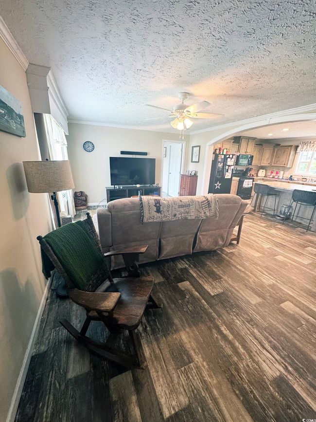 Living room with crown molding, wood finished floors, ceiling fan, and a textured ceiling | Image 9