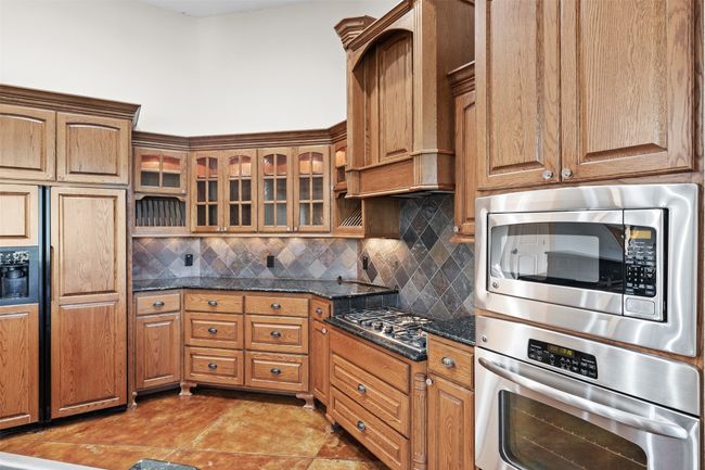 Kitchen featuring stainless steel appliances, custom range hood, tasteful backsplash, glass insert cabinets, and dark stone countertops | Image 10