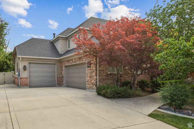View of front of home with an attached garage, driveway, roof with shingles, a gate, and stone siding | Image 70