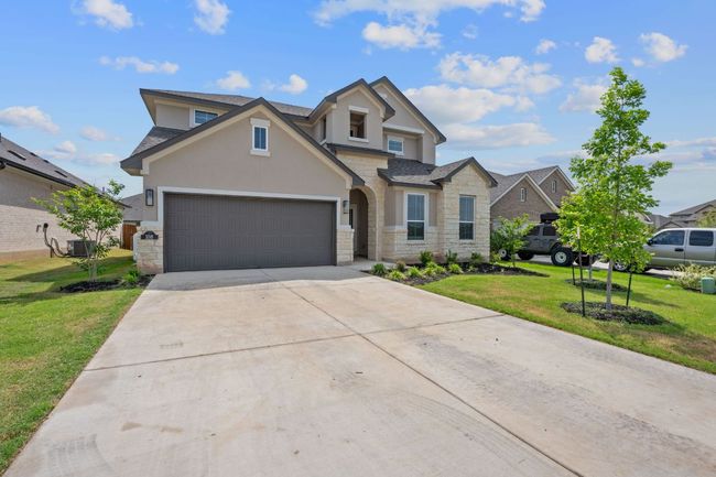 Traditional-style house featuring a front lawn, driveway, stone siding, an attached garage, and stucco siding | Image 26