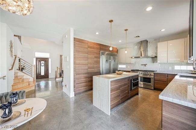 Kitchen with a center island, modern cabinets, wall chimney range hood, high end appliances, and finished concrete floors | Image 15