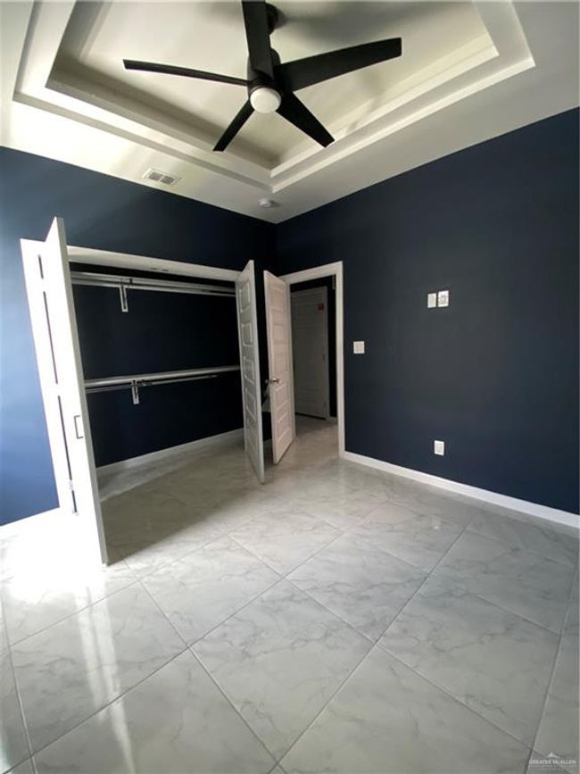 Unfurnished bedroom featuring a tray ceiling, marble look tile flooring, and ceiling fan | Image 11