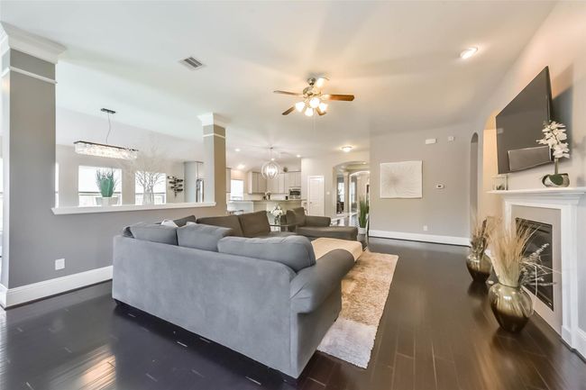 The spacious living area features an open floor plan with a cozy fireplace, modern ceiling fan, and sleek dark wood flooring. The room flows seamlessly into the dining and kitchen areas, which are brightened by large windows and contemporary lighting. Perfect for entertaining and family gatherings. | Image 9