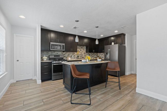 Kitchen featuring appliances with stainless steel finishes, light countertops, light wood finished floors, a kitchen breakfast bar, and recessed lighting | Image 26