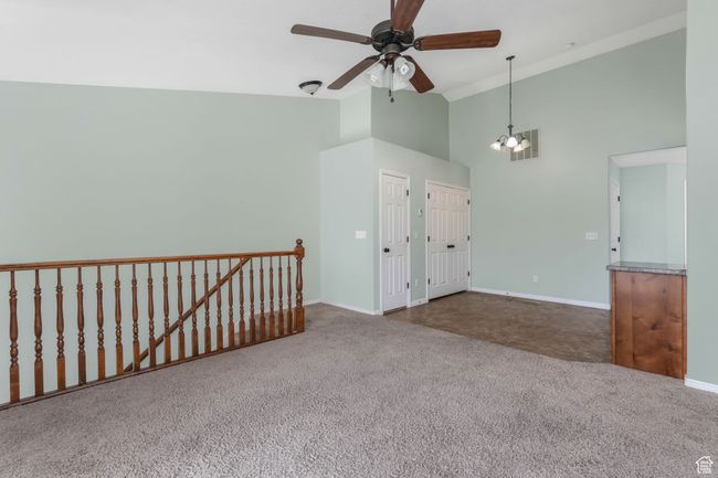 Carpeted empty room featuring high vaulted ceiling, ceiling fan with notable chandelier, baseboards, and visible vents | Image 4