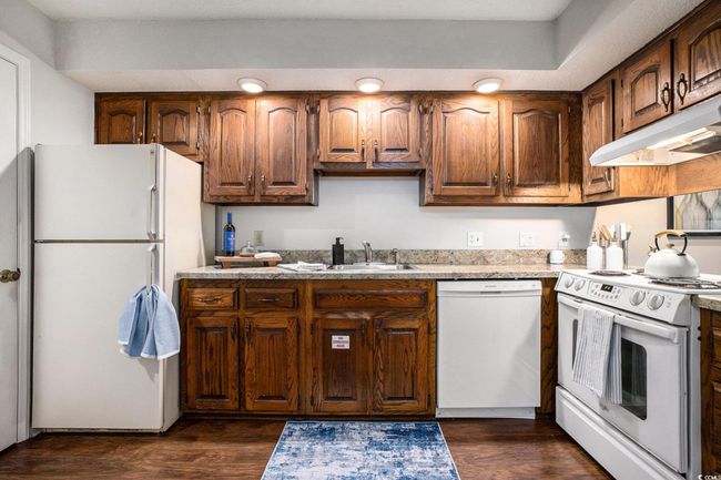 Kitchen featuring white appliances, dark wood-style floors, light countertops, under cabinet range hood, and brown cabinets | Image 9
