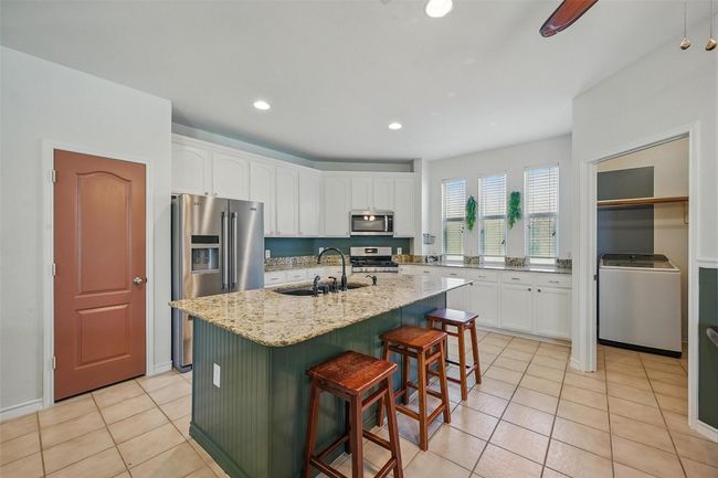 Kitchen featuring appliances with stainless steel finishes, a sink, washer / dryer, white cabinets, and light tile patterned floors | Image 9