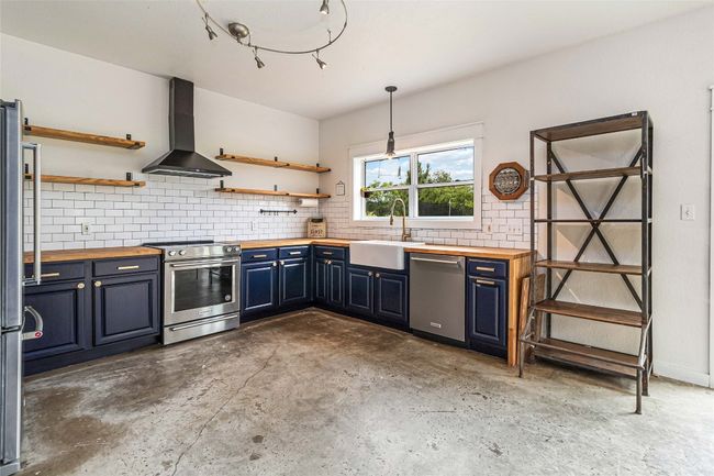 Kitchen with wall chimney range hood, wood counters, stainless steel appliances, and a sink | Image 12