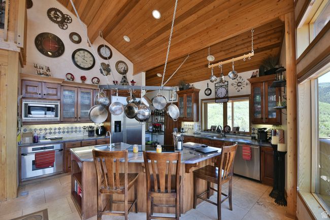Kitchen with a kitchen island with sink, built in appliances, a wealth of natural light, wooden ceiling, and backsplash | Image 76