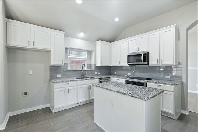 Kitchen with white cabinets, decorative backsplash, vaulted ceiling, appliances with stainless steel finishes, and a kitchen island | Image 22