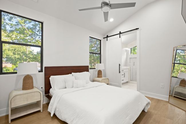 Bedroom with a barn door, lofted ceiling, light wood finished floors, ensuite bath, and ceiling fan | Image 19