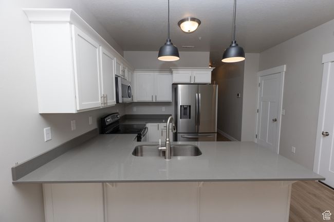 Kitchen featuring appliances with stainless steel finishes, a sink, a peninsula, hanging light fixtures, and white cabinetry | Image 8