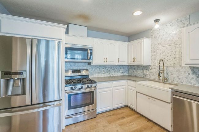 Kitchen featuring stainless steel appliances, decorative backsplash, white cabinetry, light wood-style flooring, and a textured ceiling | Image 11