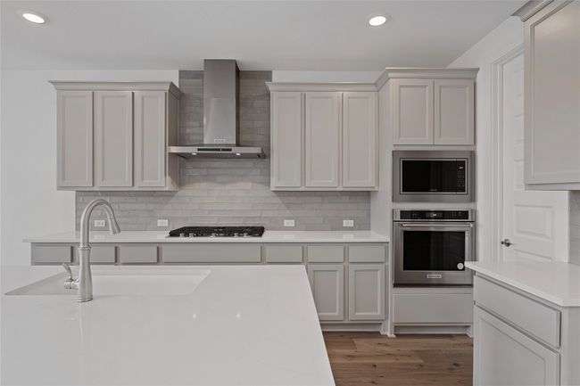 Kitchen featuring stainless steel appliances, wall chimney exhaust hood, a sink, light countertops, and backsplash | Image 6