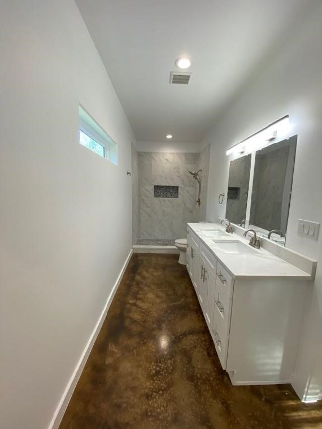 Full bath featuring a tile shower, toilet, vanity, concrete floors, and baseboards | Image 19