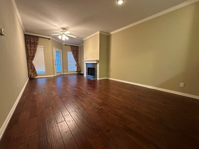 Unfurnished living room with dark wood finished floors, a ceiling fan, a fireplace, and crown molding | Image 5
