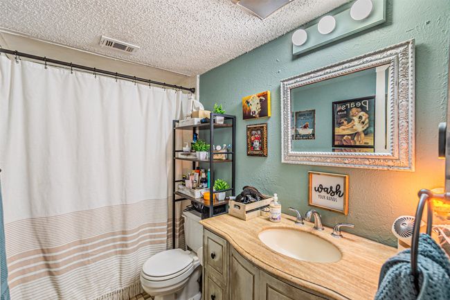 Full bathroom featuring a textured wall, toilet, vanity, a textured ceiling, and a shower with shower curtain | Image 12