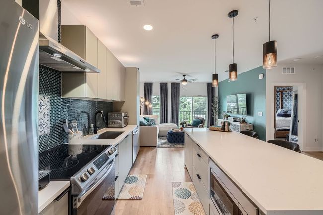 Kitchen featuring appliances with stainless steel finishes, wall chimney range hood, open floor plan, light wood-style floors, and decorative backsplash | Image 10