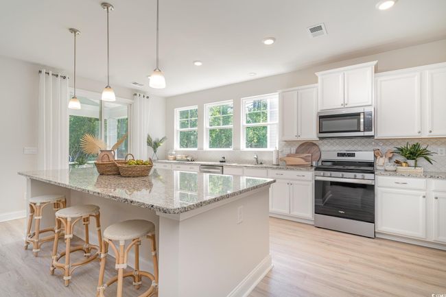Kitchen featuring light wood-style flooring, a kitchen island, appliances with stainless steel finishes, white cabinets, and decorative backsplash | Image 6