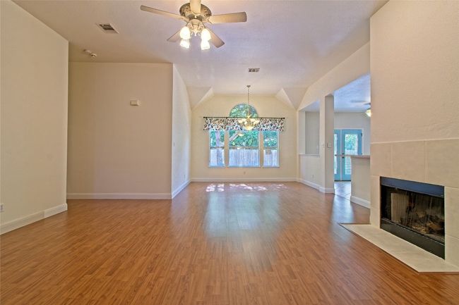 Unfurnished living room featuring a tiled fireplace, wood finished floors, a ceiling fan, a chandelier, and vaulted ceiling | Image 10