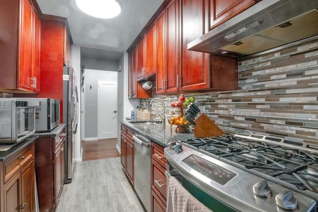 Kitchen with stainless steel appliances, exhaust hood, light wood-style flooring, and decorative backsplash | Image 10