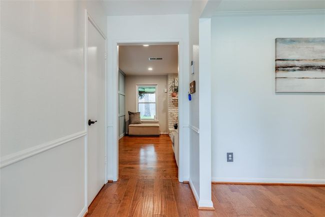This photo showcases a bright hallway with wooden flooring, leading to a cozy seating area by the fire, walls are painted neutral throughout | Image 6