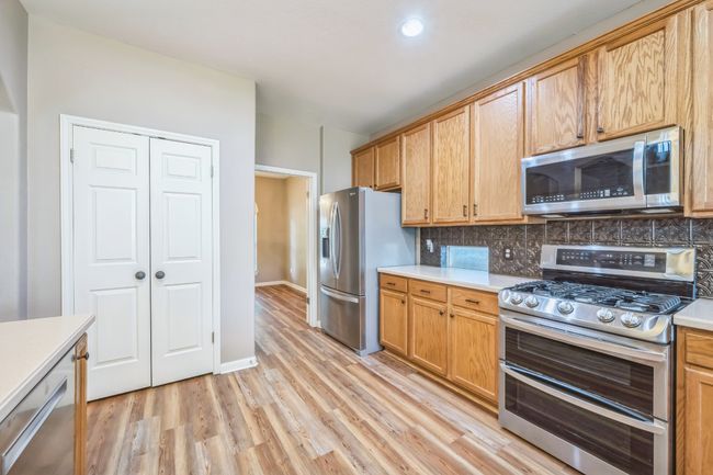 Kitchen featuring stainless steel appliances, light countertops, decorative backsplash, and light wood-style floors | Image 13