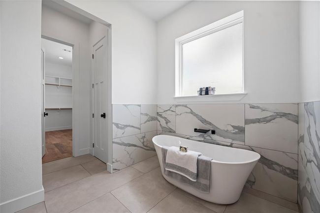 Luxurious primary bathroom featuring a freestanding tub, elegant marble accents, and abundant natural light for a serene retreat. | Image 25