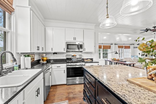 Kitchen with appliances with stainless steel finishes, white cabinetry, decorative light fixtures, light wood-style flooring, and tasteful backsplash | Image 7