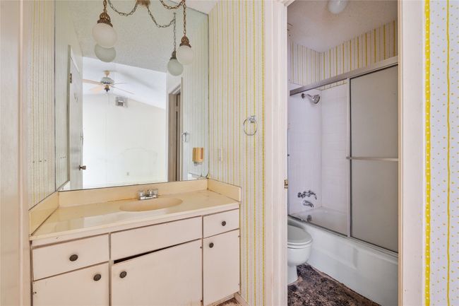 Bathroom with wallpapered walls, vanity, a ceiling fan, and shower / bath combination with glass door | Image 8