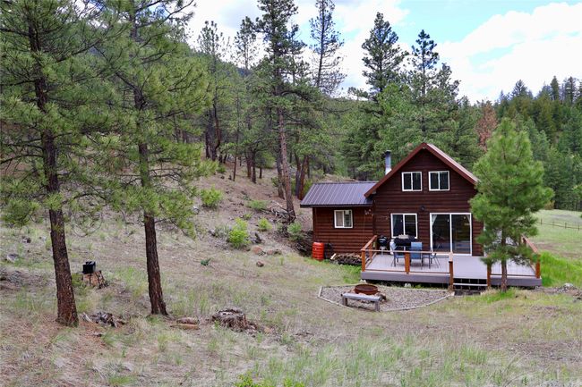 Rear view of house with a deck, metal roof, a wooded view, an outdoor fire pit, and faux log siding | Image 21