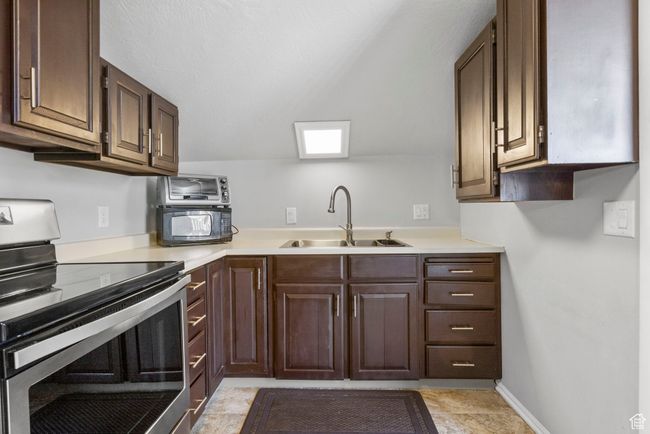 Kitchen featuring dark brown cabinets, light countertops, a sink, and stainless steel electric stove | Image 7