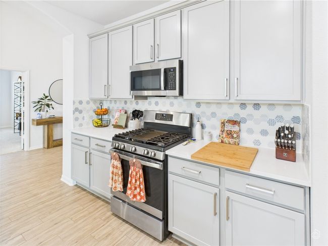 Kitchen featuring appliances with stainless steel finishes, light countertops, tasteful backsplash, light wood finished floors, and gray cabinetry | Image 9